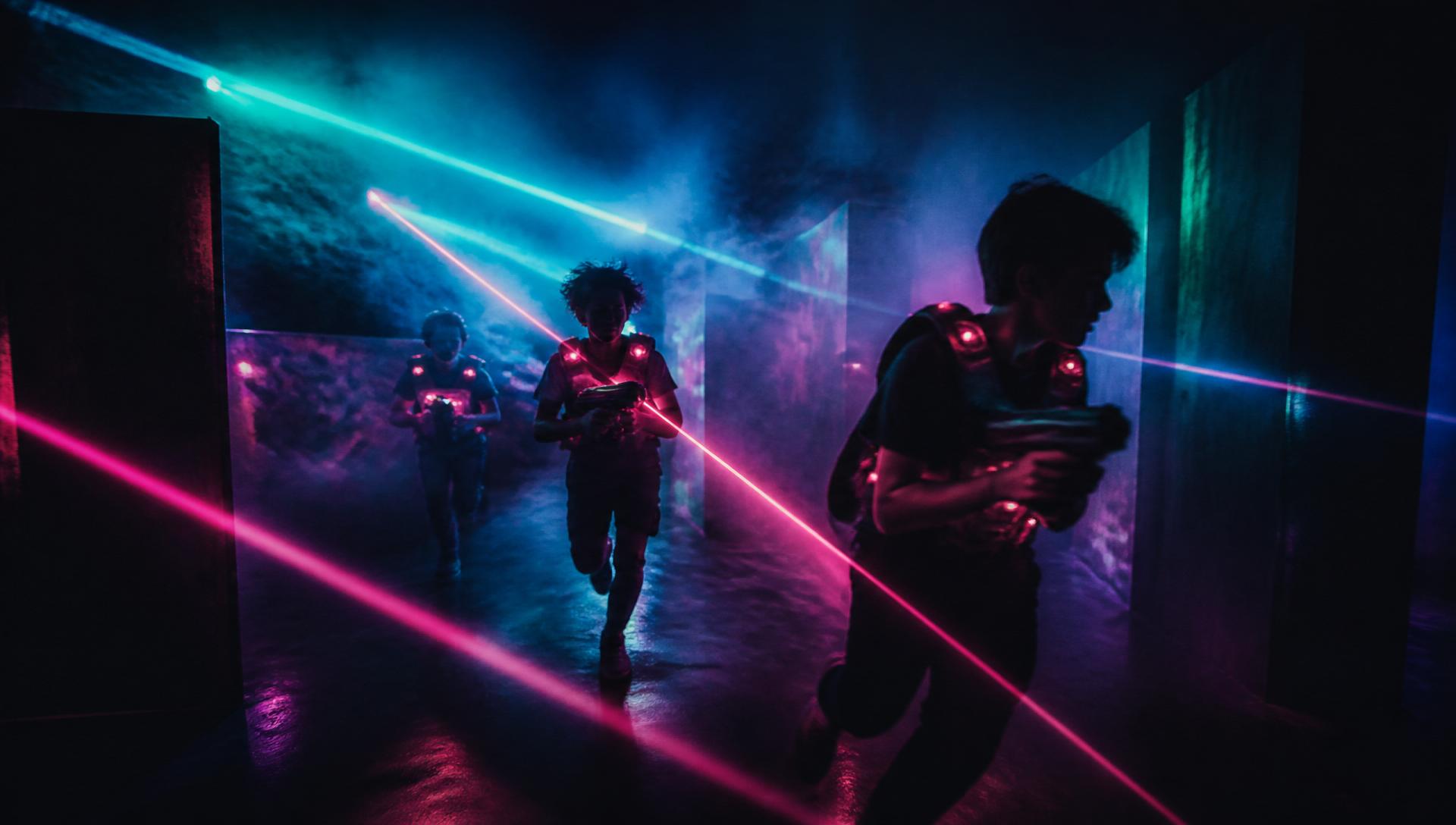 Dunkle Lasertag-Arena mit Cyan- und Magenta-Laserstrahlen und Jugendlichen in Action